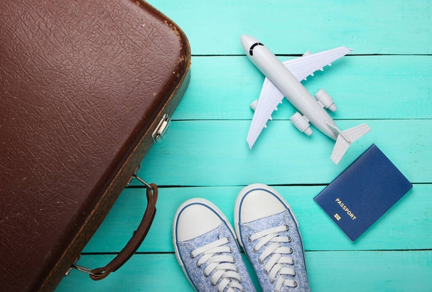 Концепция путешествия. Старый багаж, статуэтка самолета, паспорт, кроссовки на голубом деревянном полу. Полет, поездка, путешествие. Плоская композиция. Вид сверху - Фото, изображение