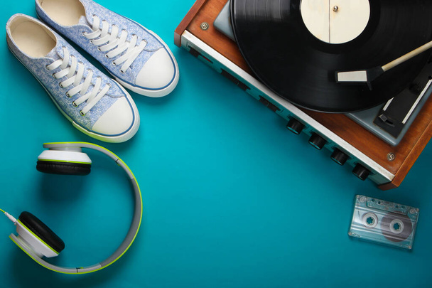 Старый виниловый проигрыватель с стерео наушниками, аудиокассетой и кроссовками на синем фоне. Ретро медиа. Вид сверху. Плоский лежал - Фото, изображение