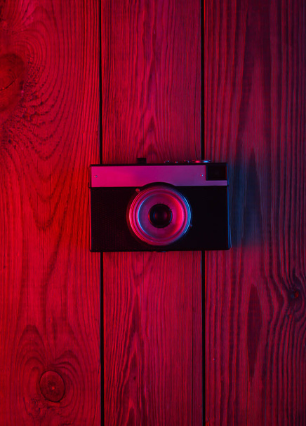 Retro camera on wooden background. Neon red blue light. Gradient glow. Top view - Photo, Image