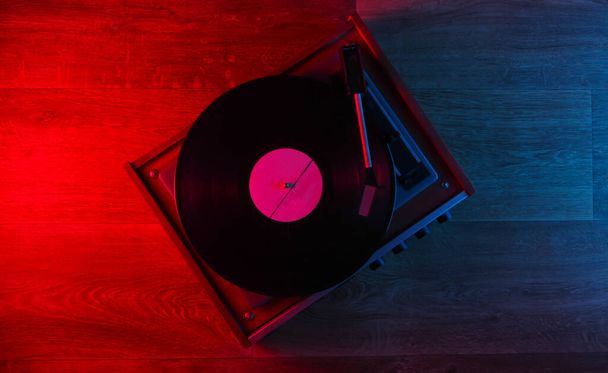 Retro gramofon winylowy na drewnianej podłodze z niebiesko-czerwonym neonem. Blask gradientu. Widok góry. DJ. - Zdjęcie, obraz