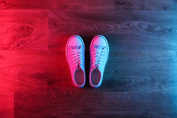 Старомодные кроссовки на деревянном полу с неоновым красно-синим градиентным свечением. Вид сверху - Фото, изображение