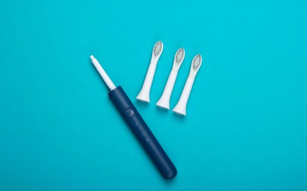 Tandverzorging. Moderne elektrische tandenborstel met mondstukken op blauwe achtergrond. Bovenaanzicht. Minimalisme - Foto, afbeelding