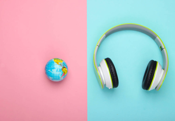 Canzone mondiale. Grafico musicale globale. La musica della terra. Cuffie stereo e un globo su sfondo blu-rosa pastello. Vista dall'alto - Foto, immagini