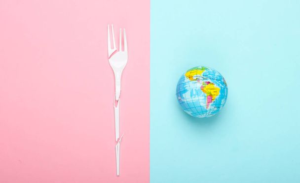 Eco still life. Save the planet concept. Plastic free. Globe and broken plastic fork on a blue-pink pastel background. Top view. Minimalism - Photo, image