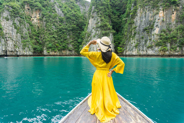 Krásná žena v jasně žluté šaty, nosí klobouk s černou mašlí, sledování krásy ostrova Phi Phi na místní longtail lodi, Krabi, Thajsko. - Fotografie, Obrázek
