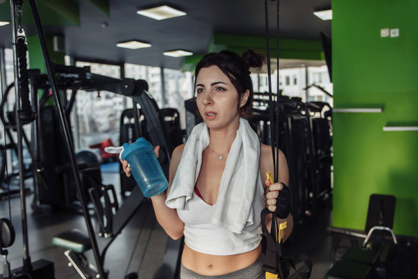 Zmęczona młoda kobieta trzymająca butelkę wody w siłowni - Zdjęcie, obraz