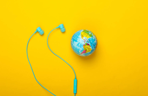 Wereldlied. Wereldwijde muziekkaart. De muziek van de aarde. Stereo oortjes en een wereldbol op gele achtergrond. Bovenaanzicht - Foto, afbeelding