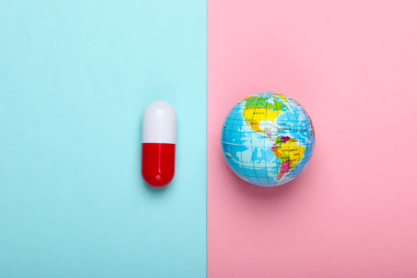 Weltweite Pandemie. Globale Epidemie. Globus und Kapselpille auf blaurosa Pastellgrund. Ansicht von oben. Minimalismus - Foto, Bild