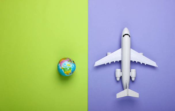 Turismo e concetto di viaggio. Emigrazione. Statuetta globo e aereo passeggero su sfondo verde viola. Vista dall'alto. Posa piatta - Foto, immagini