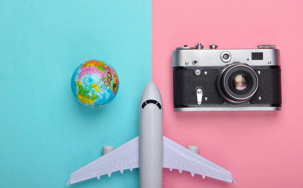 Turismo e conceito de viagem. Globo, câmera e figura de avião de passageiros em fundo pastel azul rosa. Vista superior. Depósito plano - Foto, Imagem