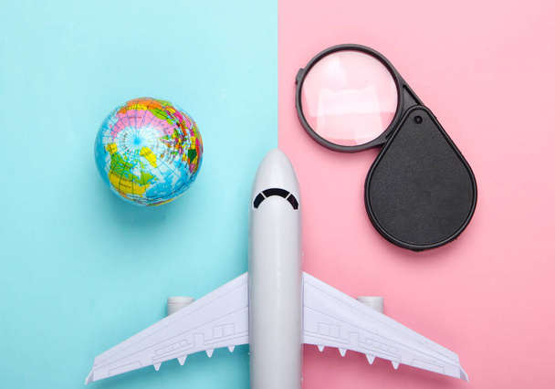 Tourism and travel concept. Globe, magnifier and passenger plane figurine on pink blue pastel background. Top view. Flat lay - Photo, Image
