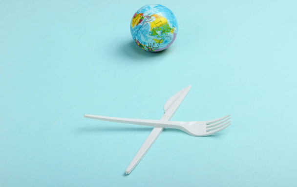 Загрязнение. Без пластика. Эко-концепция. Пластиковый нож с вилкой и глобусом на синем фоне. Спаси планету. Минимализм - Фото, изображение