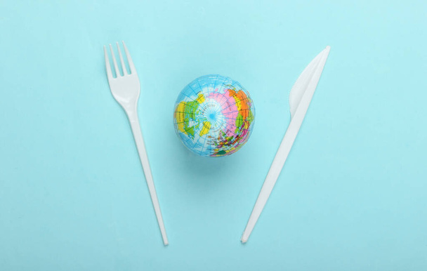 Pollution. Plastique gratuit. Concept écologique. Globe, couteau en plastique avec fourchette sur fond bleu. Sauver la planète. Vue de dessus. Minimalisme - Photo, image