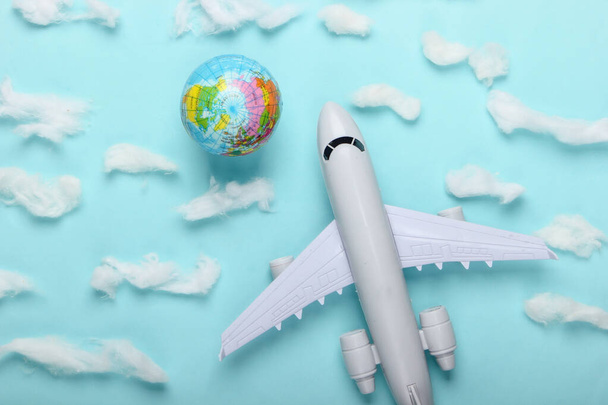 Τουρισμός και ταξιδιωτική έννοια. Globe και επιβατηγό αεροπλάνο ειδώλιο σε μπλε φόντο με σύννεφα. Μινιμαλισμός. Στο πάνω μέρος. Επίπεδη - Φωτογραφία, εικόνα