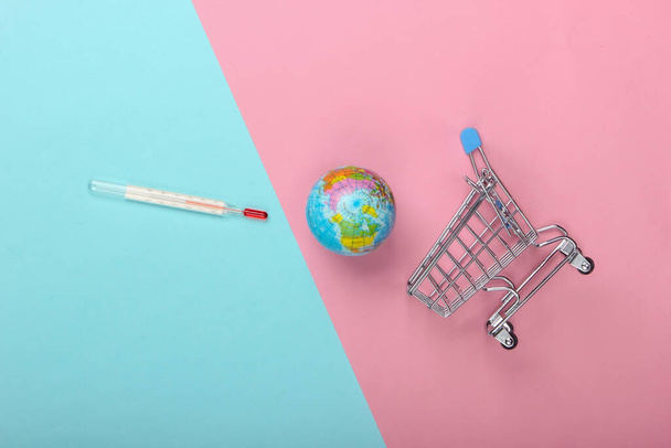 Concetto di riscaldamento globale. Carrello shopping con termometro e globo su sfondo blu-rosa pastello. Vista dall'alto, minimalismo - Foto, immagini