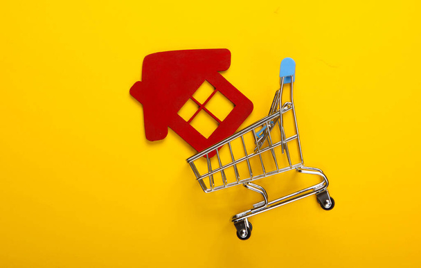 A comprar um conceito caseiro. Carrinho de compras com uma figura de casa no fundo amarelo. Vista superior - Foto, Imagem