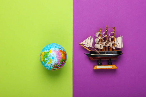 Viajar alrededor del mundo concepto. Globe, figura de barco sobre fondo verde púrpura. Vista superior. Minimalismo. Puesta plana - Foto, Imagen