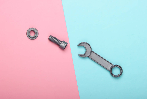Toy wrench and nut with a bolt on a blue-pink pastel background. Top view - Fotografie, Obrázek