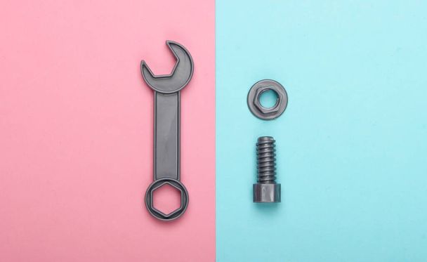 Toy wrench and nut with a bolt on a blue-pink pastel background. Top view - Zdjęcie, obraz