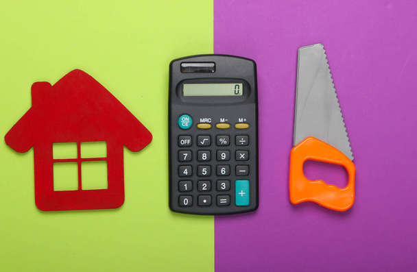 Obliczanie kosztów budowy domu lub naprawy. Figurka domu, kalkulator i piła do zabawek na zielono-fioletowym tle. Widok z góry - Zdjęcie, obraz