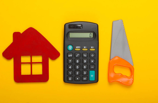 Calcul du coût de construction d'une maison ou de réparation. Figurine maison, calculatrice et scie jouet sur fond jaune. Vue du dessus - Photo, image