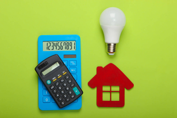 Energiatehokkuuden ja kustannusten laskeminen. Laskin, talon hahmo, led-lamppu vihreällä taustalla. Yläkuva - Valokuva, kuva