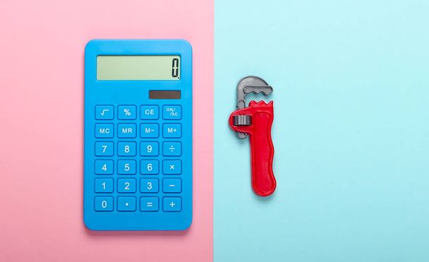 Berekening van de reparatiekosten. Calculator en speelgoedsleutel op een blauw-roze pastelachtergrond. Bovenaanzicht - Foto, afbeelding
