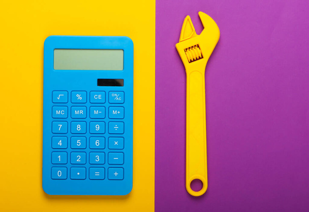 Calculation of the cost of repair work. Calculator and toy wrench on purple yellow background. Top view - Photo, Image