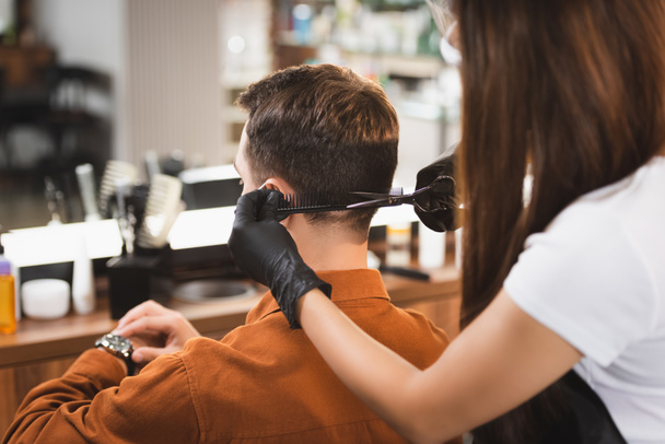 man looking at wristwatch while hairstylist on blurred foreground cutting his hair - Foto, Bild