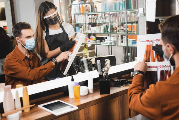 зеркальное отражение парикмахера и клиента, смотрящего на палитру цвета волос на размытом переднем плане - Фото, изображение
