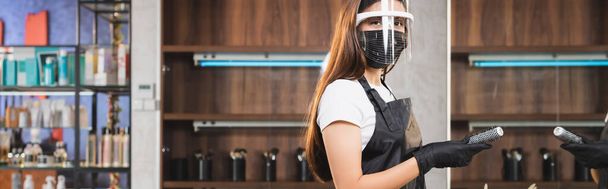 young hairdresser in face shield and latex gloves holding comb while looking at camera, banner - Foto, Bild