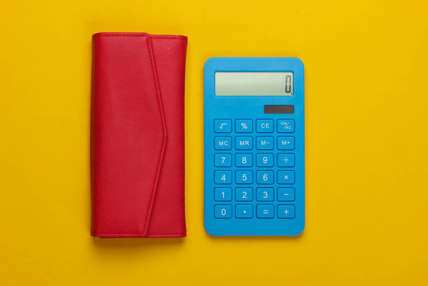 Aile bütçesini yönet. Alışveriş maliyetleri. Sarı arka planda kırmızı deri cüzdanı olan mavi hesap makinesi. Üst görünüm - Fotoğraf, Görsel