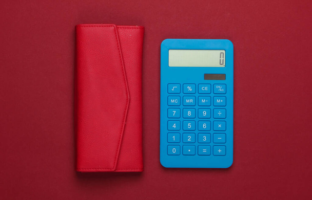 Gerenciar orçamento familiar. Custos de compras. Calculadora azul com carteira de couro vermelho no fundo vermelho. Vista superior - Foto, Imagem