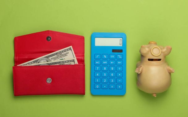 Kezelje a családi költségvetést. Bevásárlási költségek. Kék számológép, piros bőrpénztárca pénzzel és malacpersely zöld háttérrel. Felülnézet - Fotó, kép