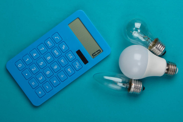 Energiebesparing. Calculator met gloeilampen op blauwe achtergrond. Bovenaanzicht - Foto, afbeelding