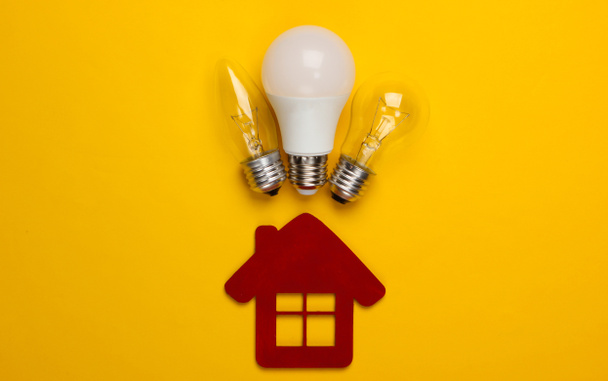 Energy saving concept. House figurine and light bulbs on yellow background. Top view - Zdjęcie, obraz