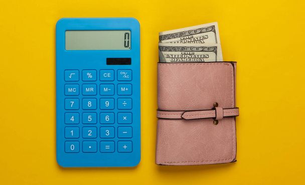 Gerenciar orçamento familiar. Custos de compras. Calculadora azul e carteira de couro com notas de dólar no fundo amarelo. Vista superior - Foto, Imagem
