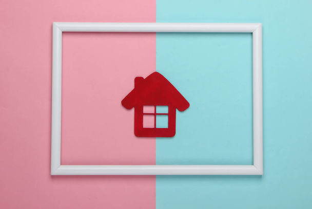 Rode Huis beeldje in wit frame op roze blauwe achtergrond. Concept kunstfoto. Bovenaanzicht. Minimalisme - Foto, afbeelding