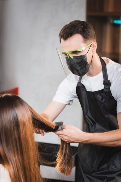 fryzjer w tarczy twarzy i fartuch czesanie włosy kobiety - Zdjęcie, obraz