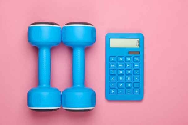 Fitness, weight loss still life. Calorie Counting. Calculator and dumbbells on a pink pastel background. Minimalism. Flat lay - Photo, Image