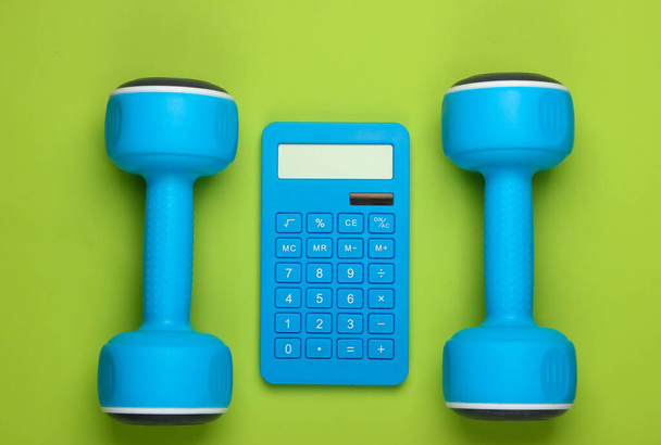 Fitness, weight loss still life. Calorie Counting. Calculator and dumbbells on green background. Minimalism. Flat lay - Photo, Image