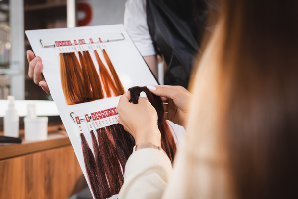 partial view of hairstylist holding hair colors palette near client on blurred foreground - Фото, изображение