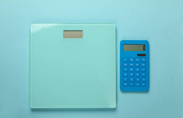 Diet, weight loss still life. Calorie Counting. Calculator and scales on blue background. Minimalism. Flat lay. Top view - Photo, Image