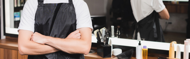 cropped view of hairdresser in apron standing with crossed arms on blurred background, banner - Photo, Image