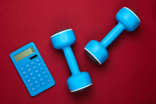 Fitness, Gewichtsverlust noch Leben. Kalorienzählen. Taschenrechner und Kurzhanteln auf rotem Hintergrund. Minimalismus. Flache Lage - Foto, Bild