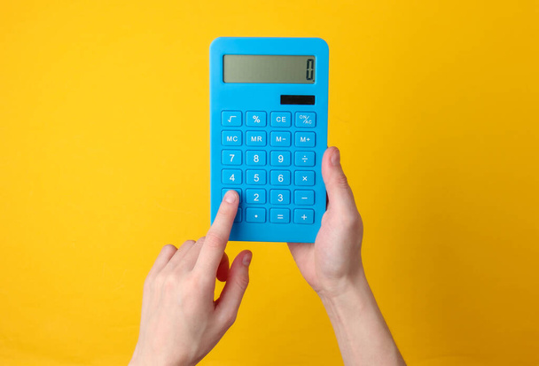 Hand houdt blauwe rekenmachine op gele achtergrond. - Foto, afbeelding