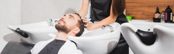 理容師は理容室で若い顧客の髪を洗うバナー - 写真・画像