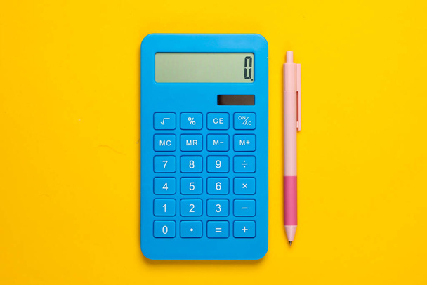 Синий калькулятор с ручкой на желтом фоне. Вид сверху. - Фото, изображение