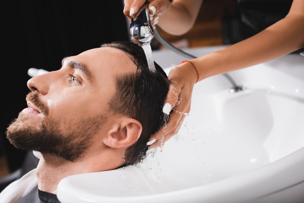 hairdresser washing hair of young, bearded client in barbershop - Foto, Imagem