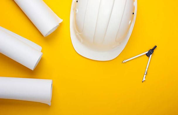 Engineering construction safety helmet, drawing rolls, compass on yellow background. Building house. Top view. Flat lay - Foto, afbeelding